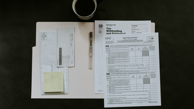 Tax forms, a pen, and a coffee mug on a dark desk