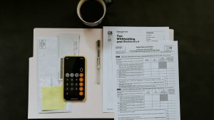 Black Android smartphone near ballpoint pen, tax withholding certificate on top of white folder