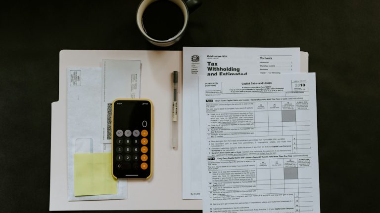 Black Android smartphone near ballpoint pen, tax withholding certificate on top of white folder