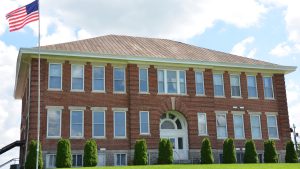 A red brick school building with a metal roof and an American flag