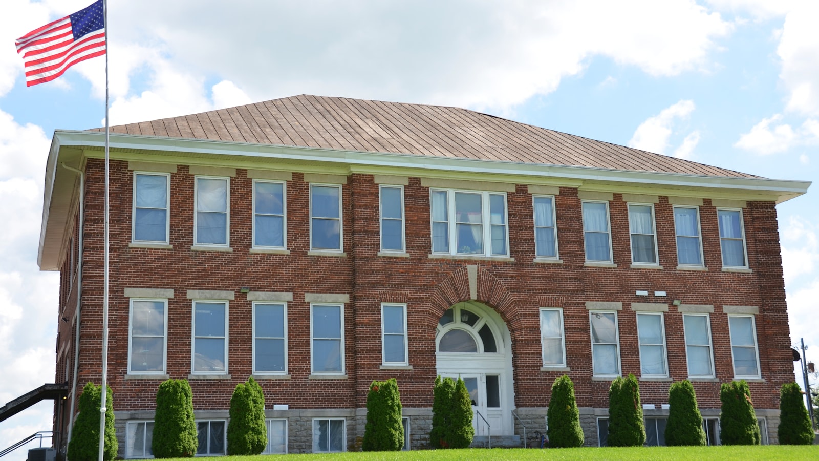 A red brick school building with a metal roof and an American flag